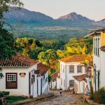 a cobblestone street with white buildings and mountains in the background